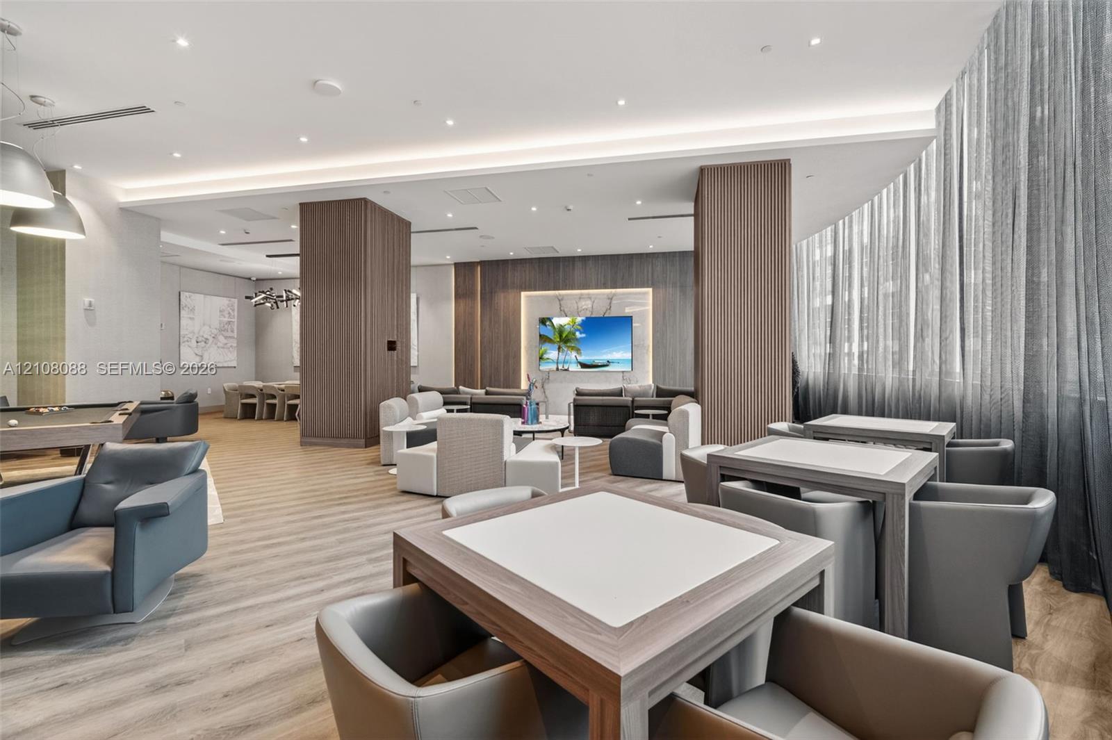 Expansive common area featuring wood-finish flooring, recessed lighting, floor-to-ceiling sheer window treatments, and wood-paneled structural columns