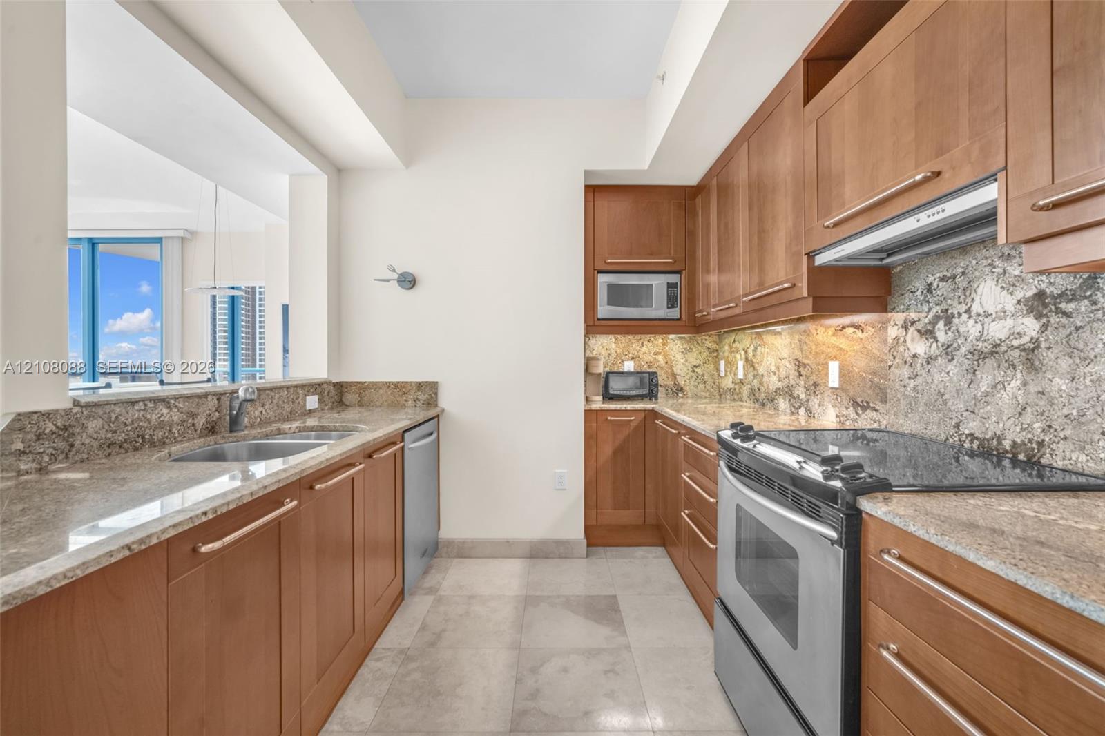 Kitchen featuring wood cabinetry, stone countertops, stone backsplash, stainless steel appliances, and large-format tile flooring Kitchen featuring wood cabinetry, stone countertops, stone backsplash, stainless steel appliances, and large-format tile flooring