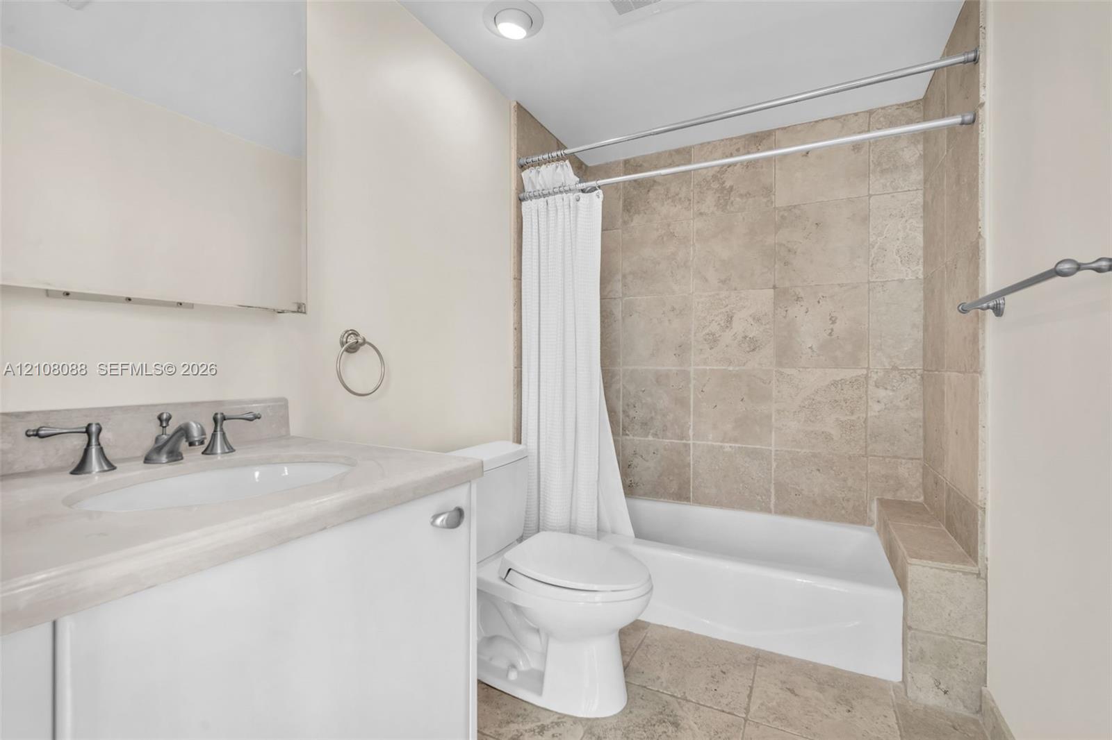 Bathroom featuring natural stone tile tub surround and flooring, vanity with stone countertop, recessed lighting, and metallic hardware