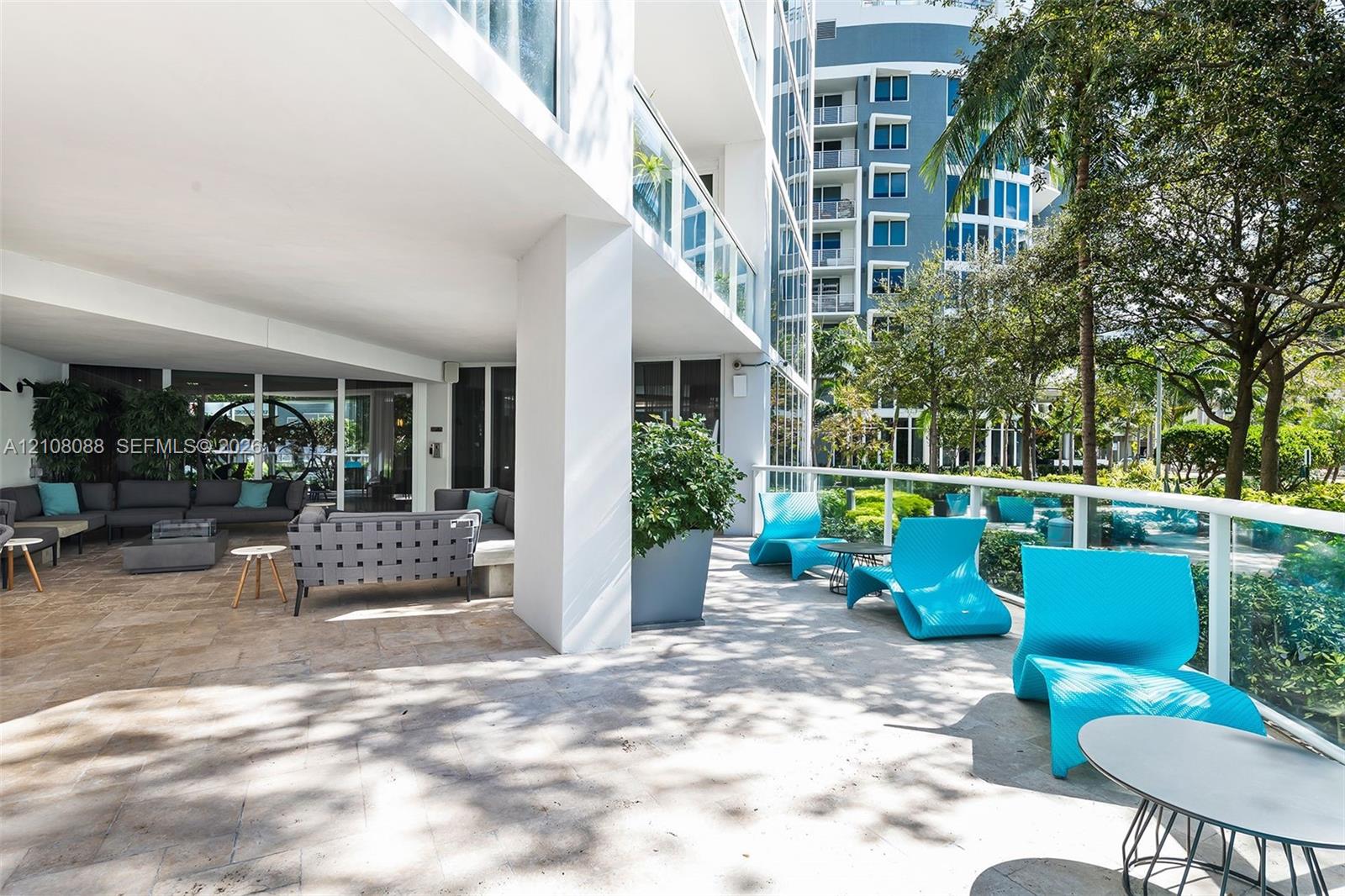 Expansive covered outdoor terrace featuring natural stone flooring, glass panel railings, and mature perimeter landscaping