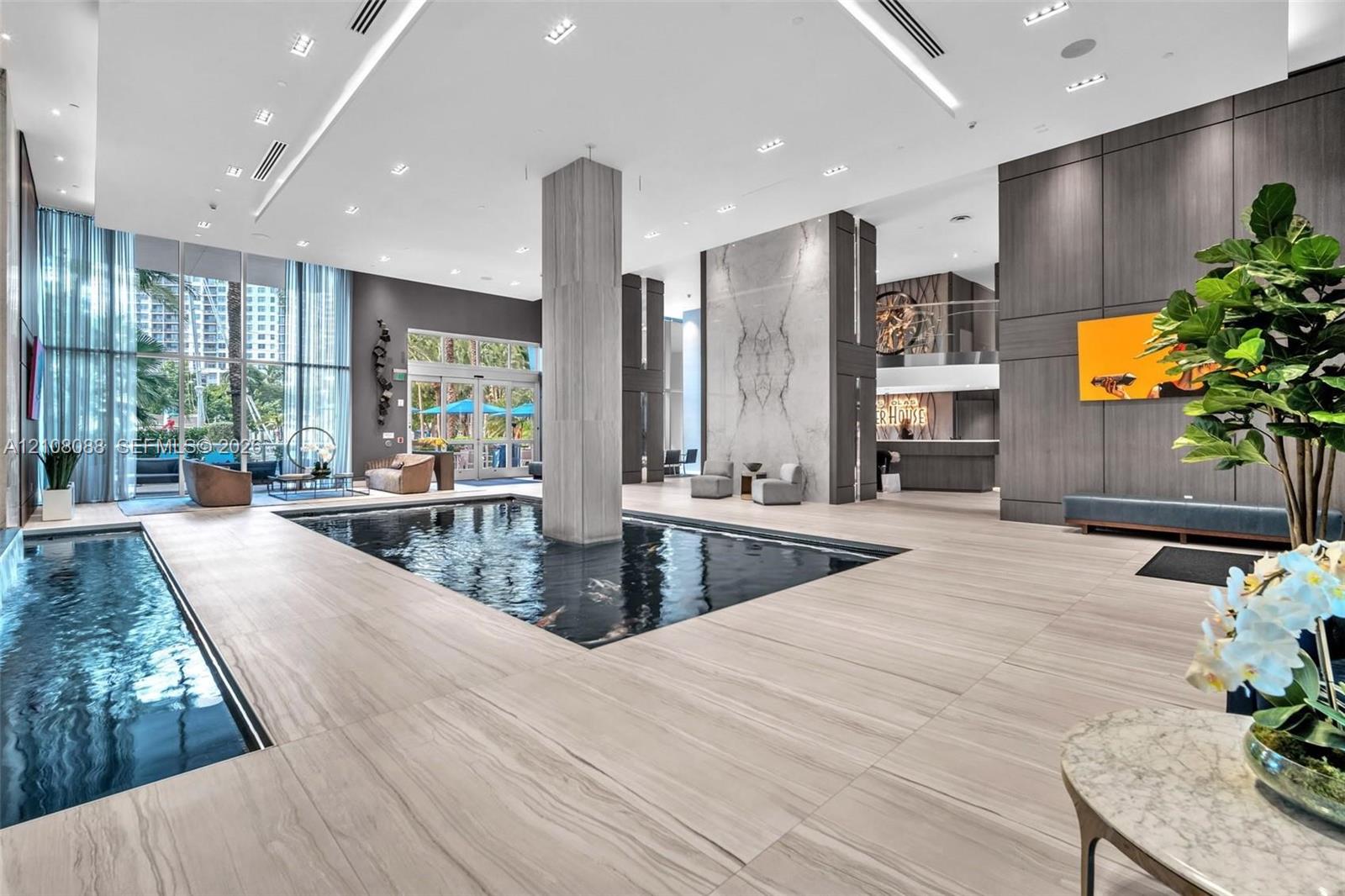 Grand lobby featuring floor-to-ceiling windows, integrated reflecting pools, stone-finish tile flooring, recessed architectural lighting, and floor-to-ceiling stone wall cladding