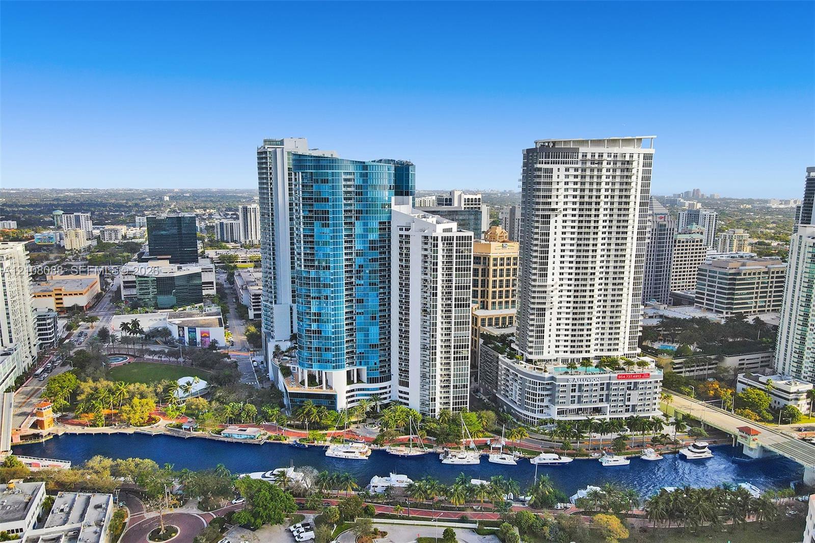 Aerial perspective featuring high-rise glass-clad architecture, a concrete waterfront promenade, and a deep-water canal supporting nautical traffic Aerial perspective featuring high-rise glass-clad architecture, a concrete waterfront promenade, and a deep-water canal supporting nautical traffic