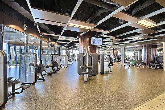Fitness facility featuring floor-to-ceiling windows, exposed industrial ceiling with wood-panel accents, wall-to-wall resilient flooring, and wood-paneled structural columns