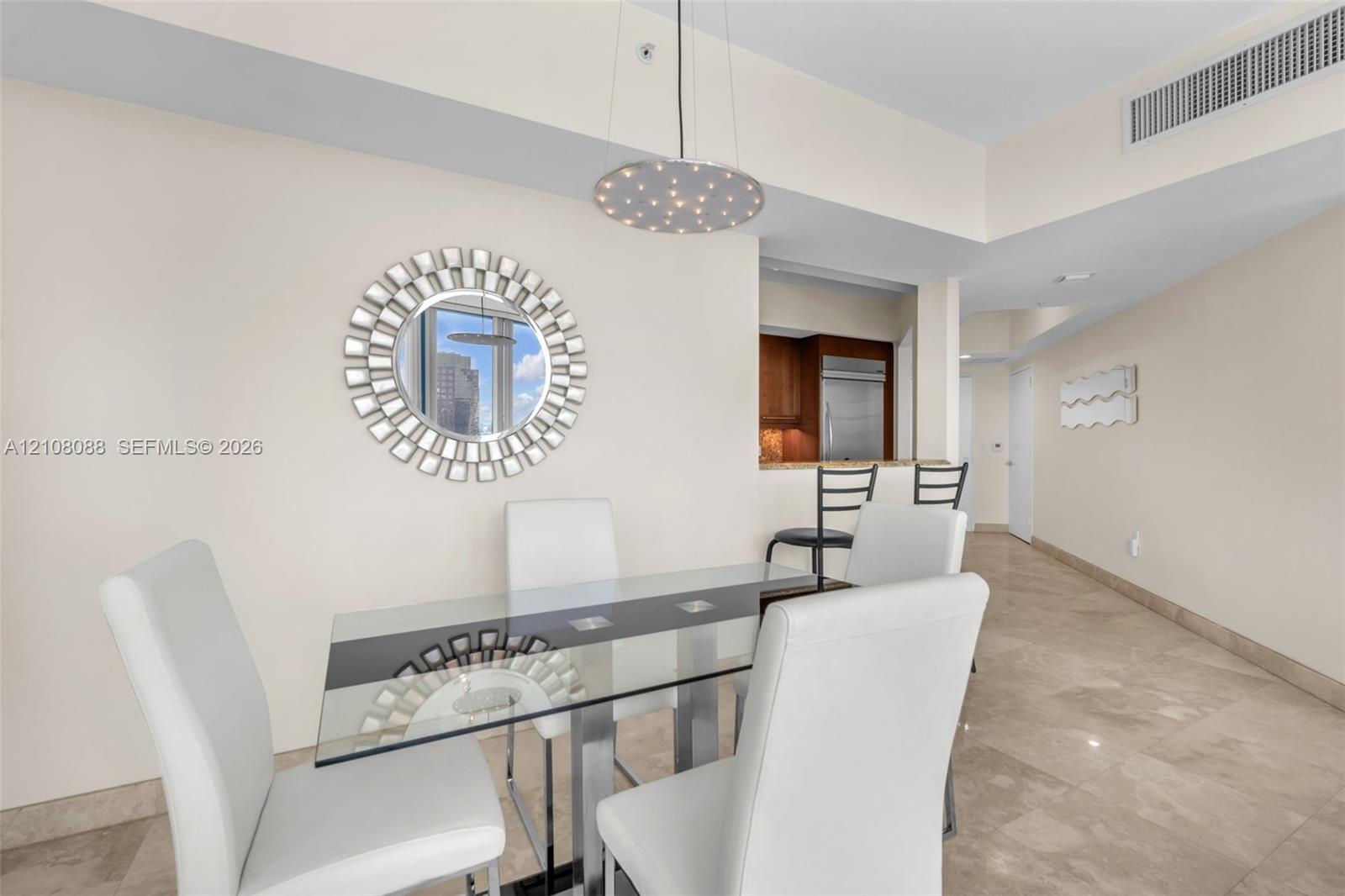Polished stone tile flooring, circular decorative wall mirror, contemporary circular pendant light, and pass-through opening with stone-topped breakfast bar