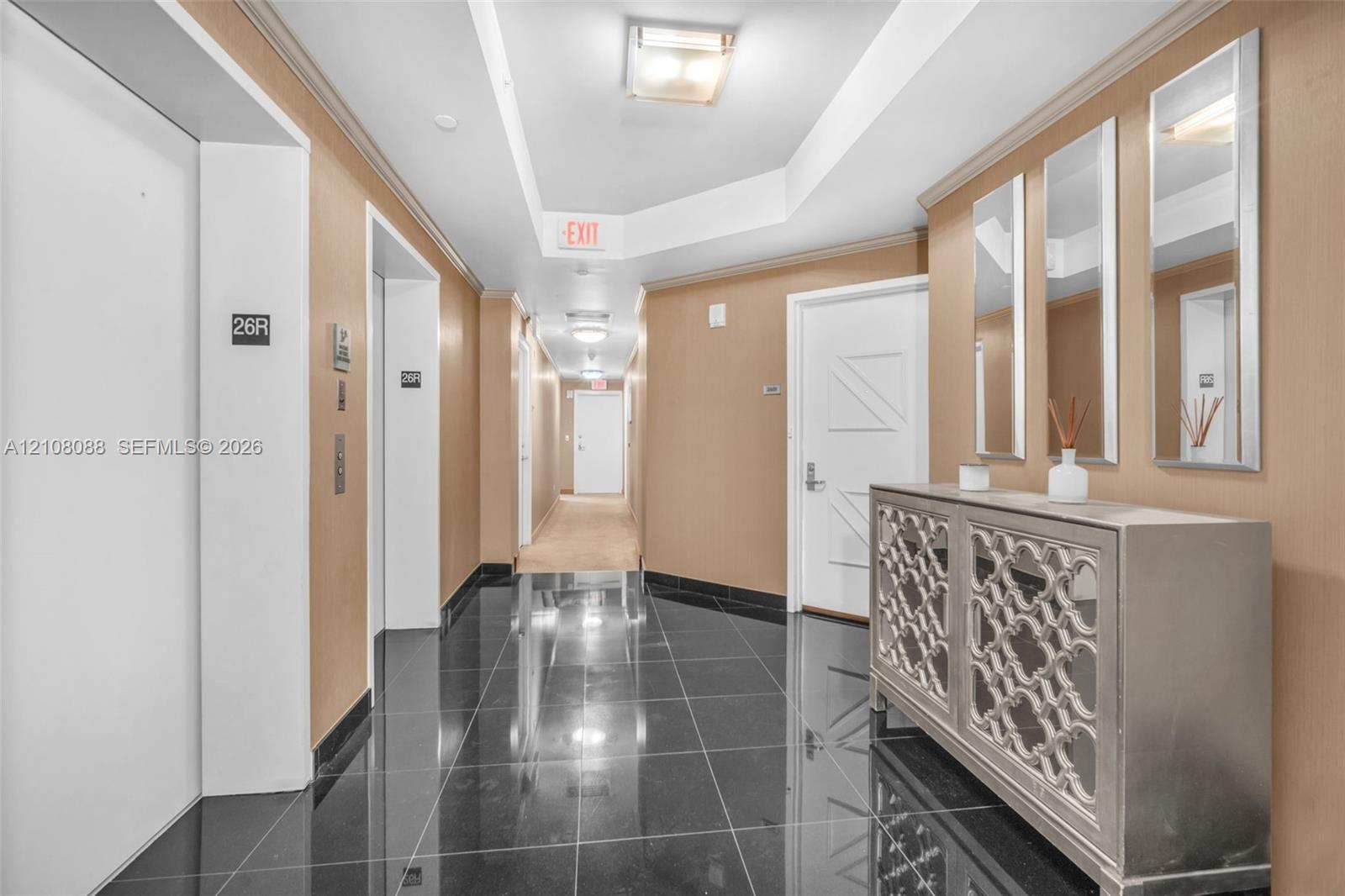 Polished black stone flooring, tray ceiling with recessed lighting, and wall-mounted flush-mount fixtures