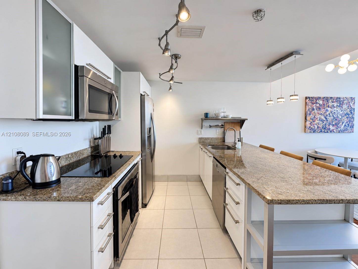 Kitchen featuring white flat-panel cabinetry with frosted glass inserts, stone countertops, stainless steel appliances, tile flooring, and adjustable track lighting