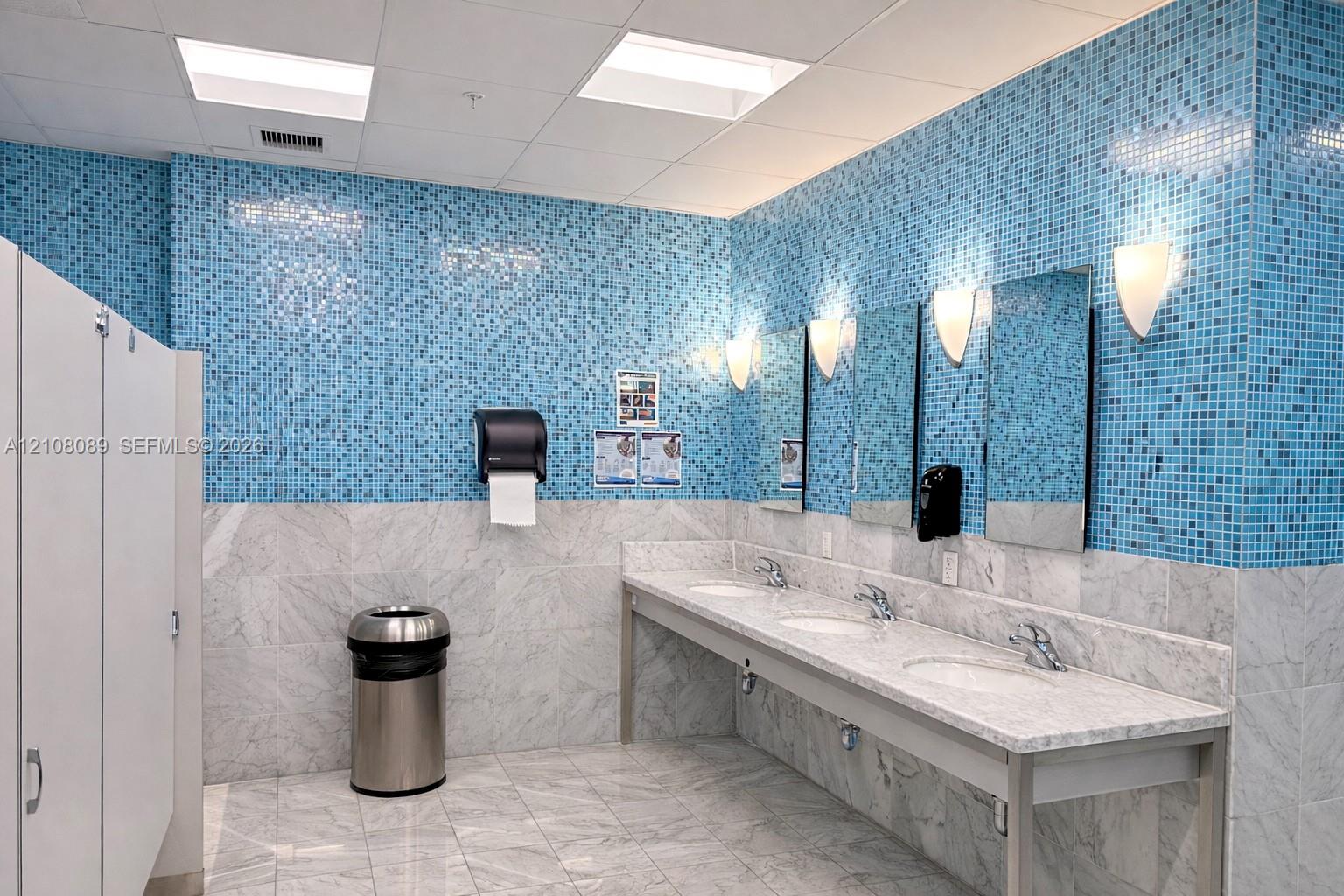 Multi-station stone vanity with integrated sinks, polished stone flooring, blue mosaic tile wall accents, and wall-mounted sconce lighting