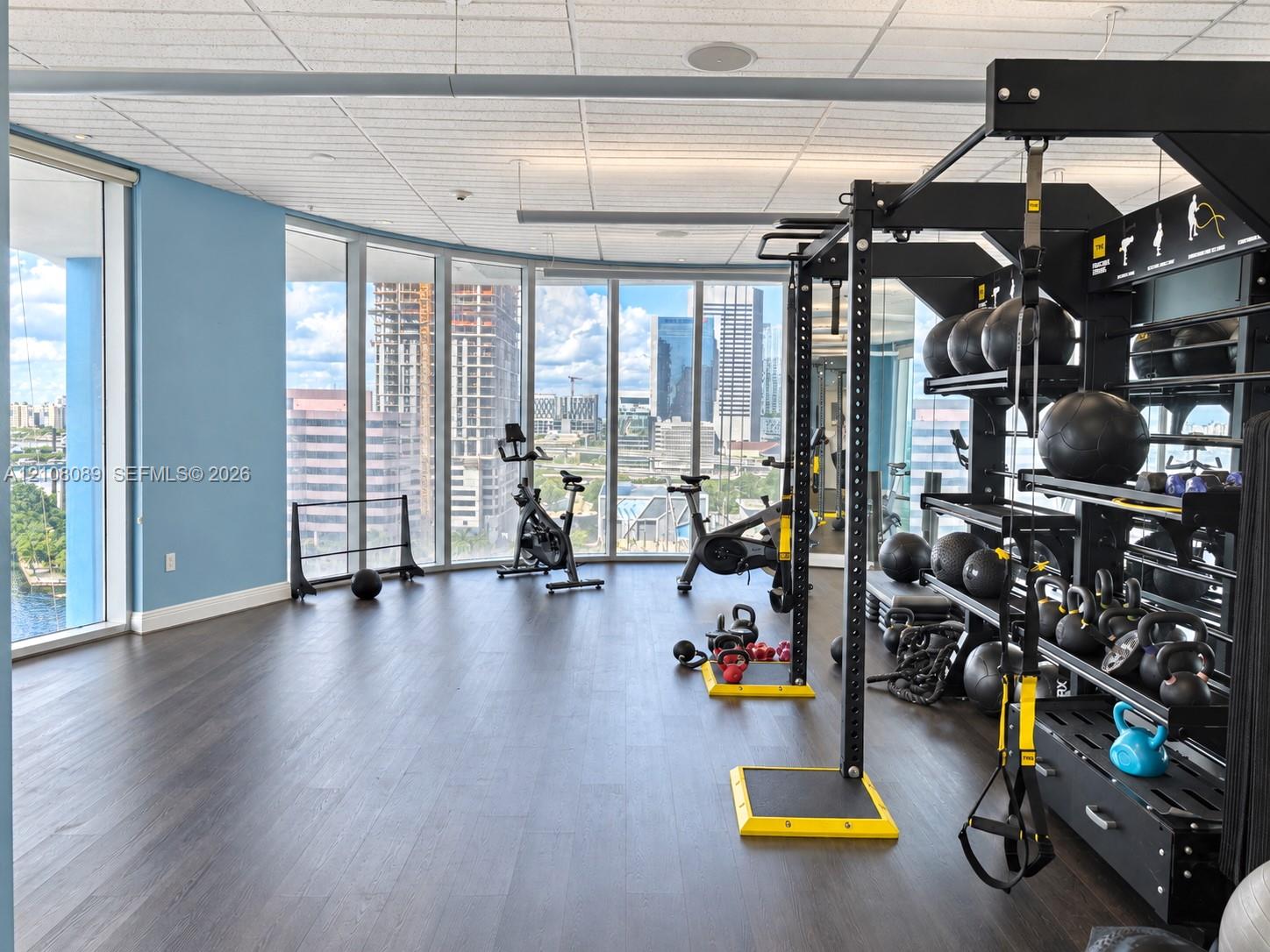 Floor-to-ceiling windows featuring urban scenery, wood-finish flooring, and recessed ceiling lighting