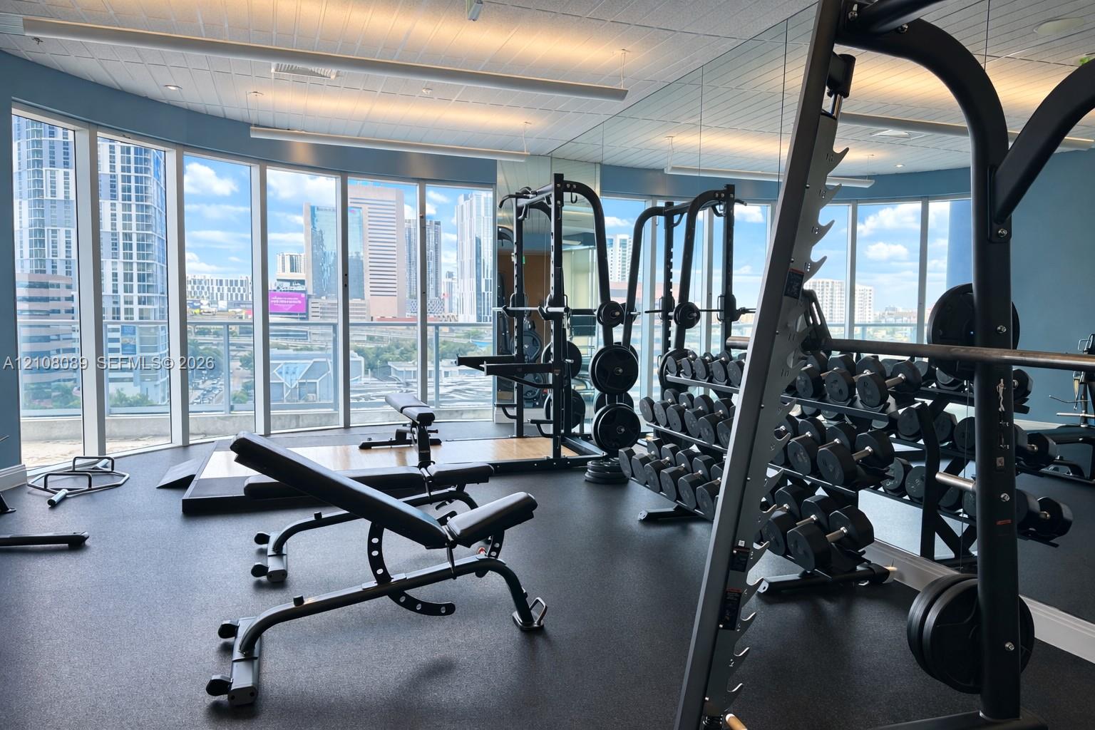 Fitness center featuring floor-to-ceiling windows, panoramic urban scenery, and mirrored walls