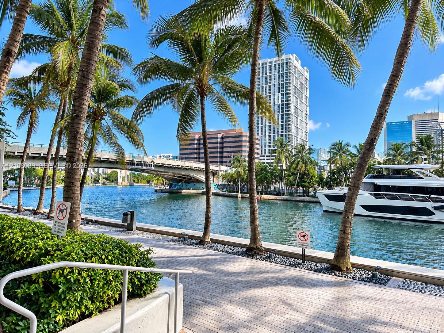 Waterfront promenade featuring stone paver walkways, mature palm trees, and bulkhead retaining walls along a waterway