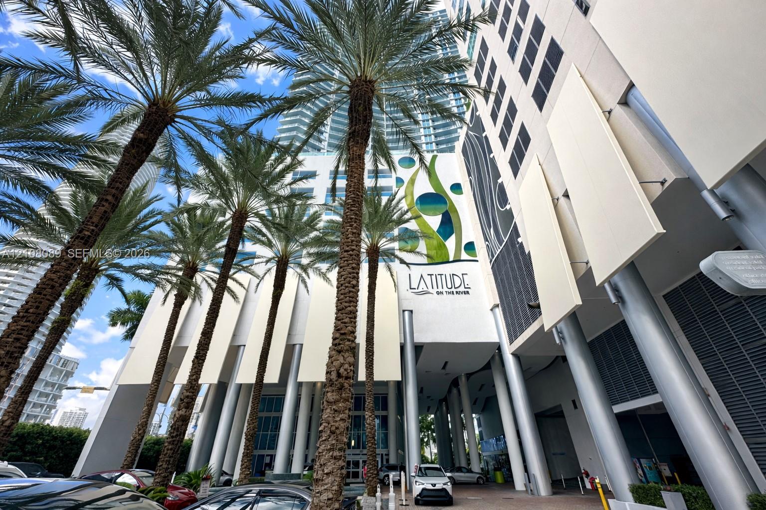 High-rise exterior featuring a concrete facade, prominent structural pillars, decorative vertical panels, and mature palm trees