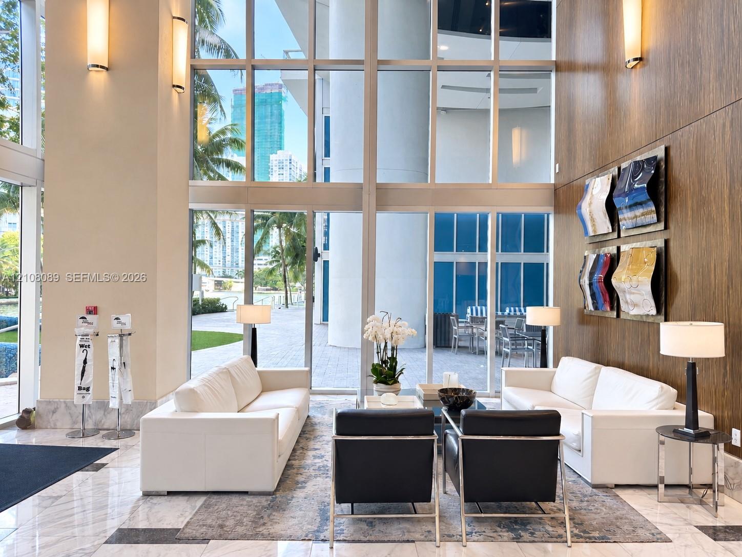 Double-height floor-to-ceiling windows, polished stone flooring, wood-paneled feature wall, and wall-mounted metal light fixtures