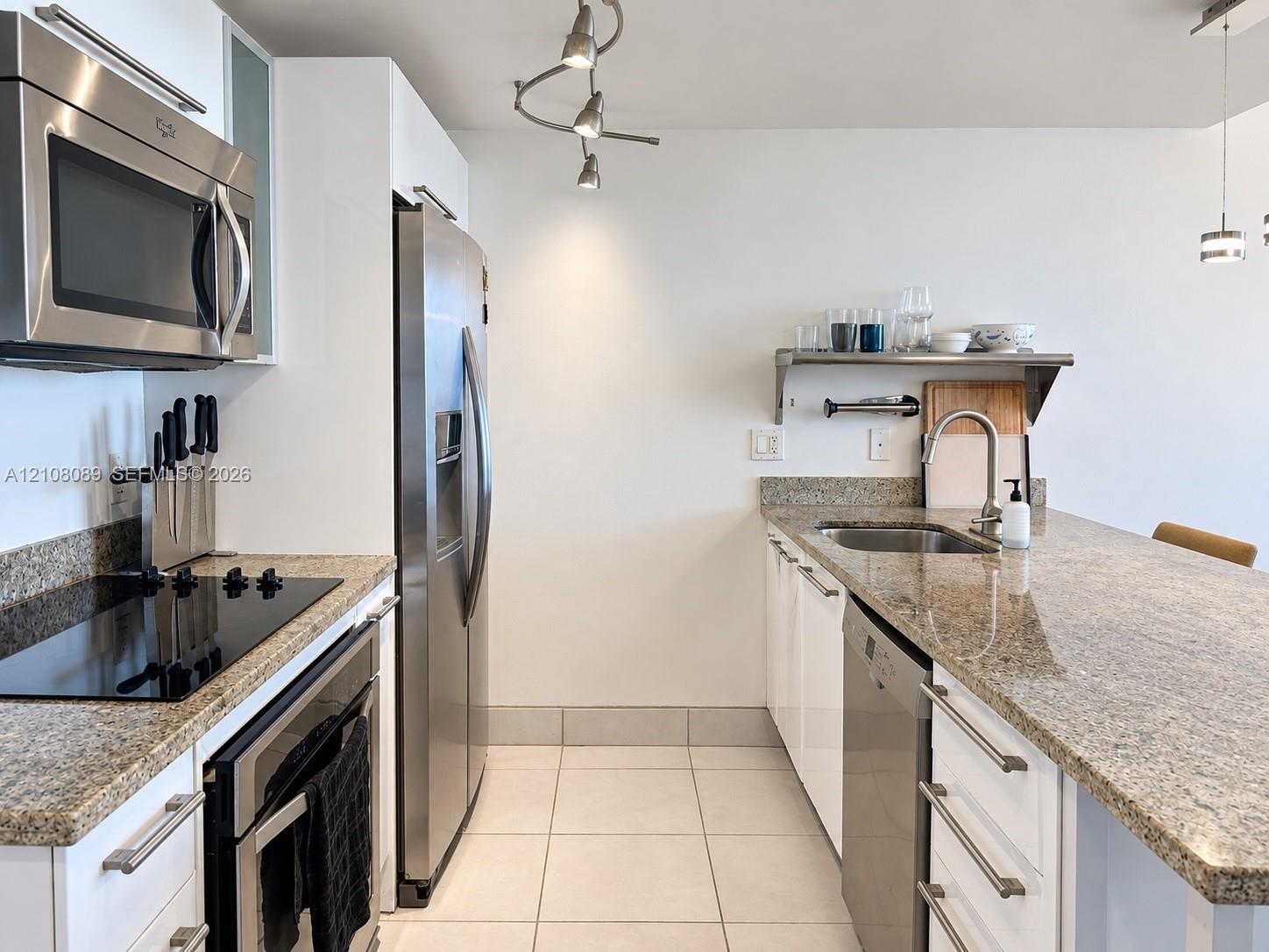 Kitchen featuring stone countertops, stainless steel appliances, white cabinetry, a built-in wall-mounted shelf, and tile flooring