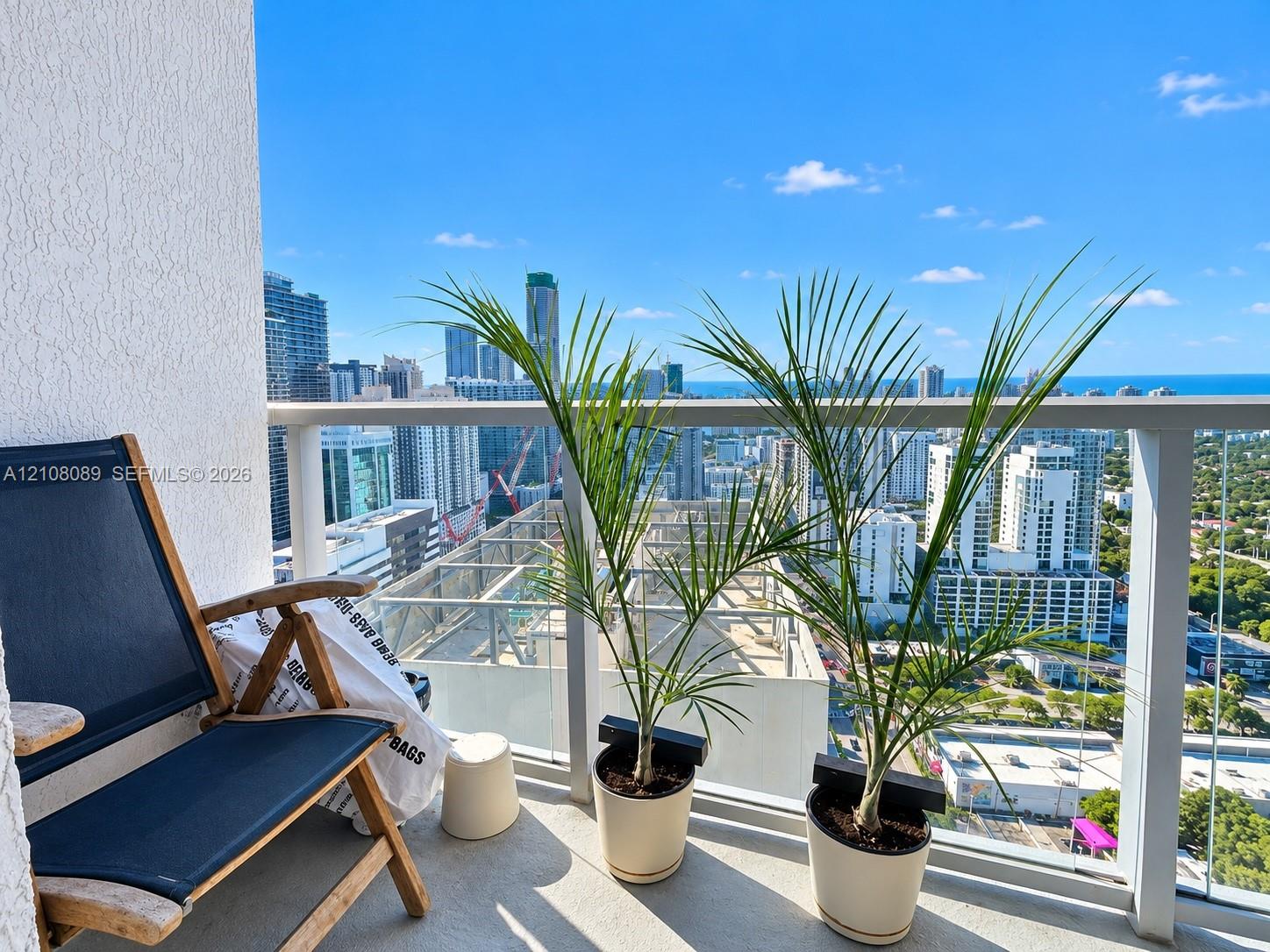 Private balcony featuring a glass panel railing and concrete flooring, overlooking the metropolitan skyline and coastline
