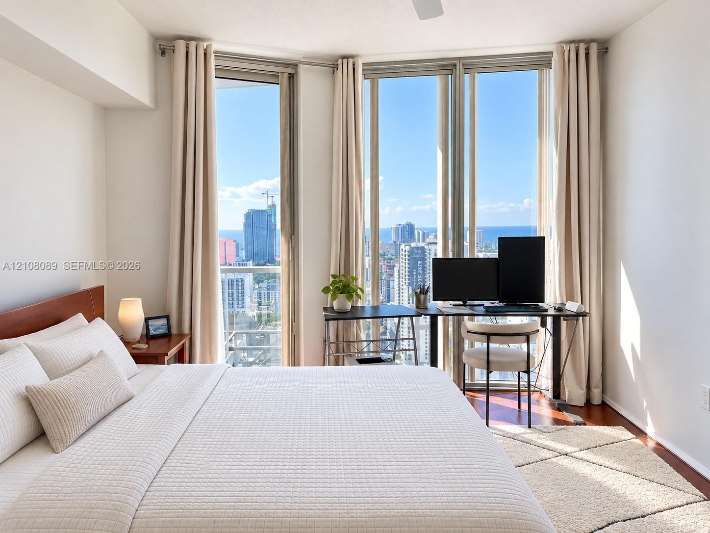 Floor-to-ceiling windows featuring urban and coastal scenery, wood-finish flooring, and a ceiling fan