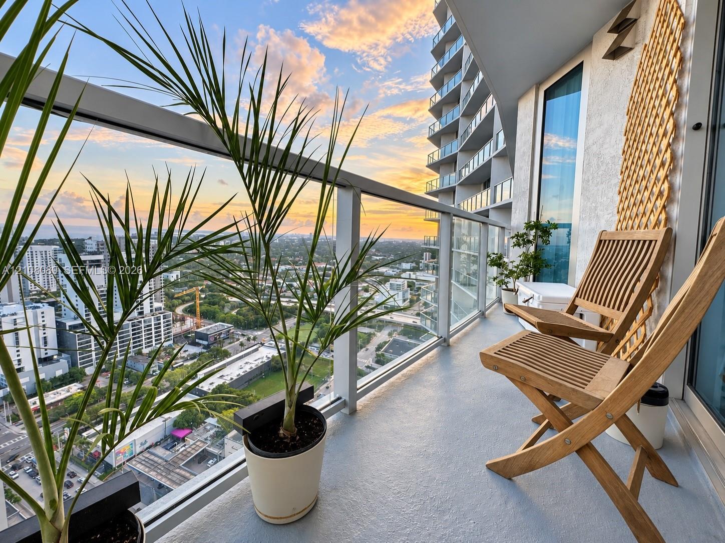 Covered balcony featuring glass railing, metal framework, and concrete flooring with sunset horizon backdrop