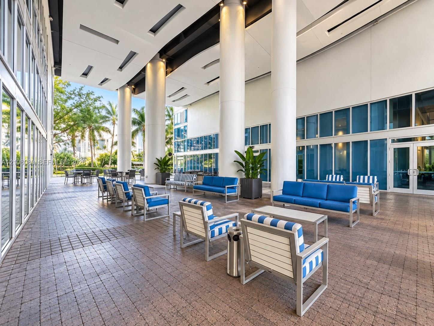 Covered outdoor terrace featuring a paver stone floor, full-height glass walls, and structural cylindrical columns with recessed ceiling lighting