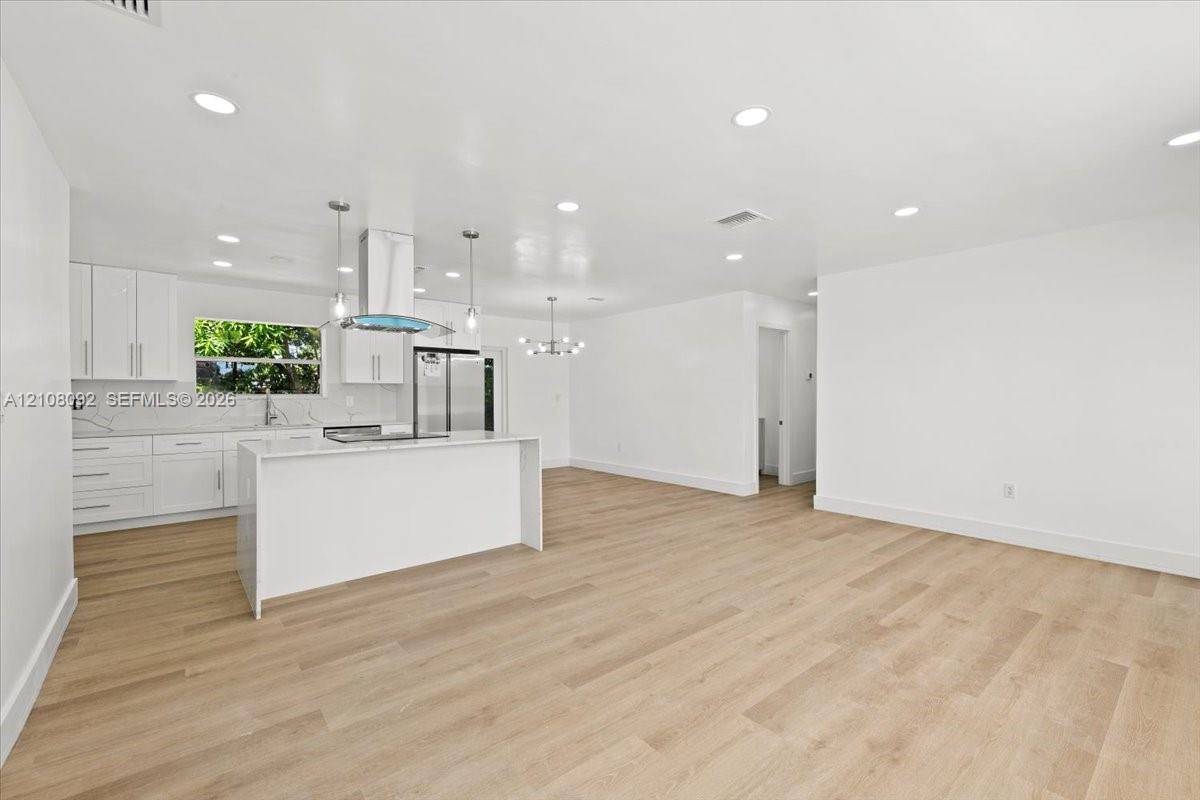 Kitchen featuring white shaker-style cabinetry, an island with a stone-finish countertop, stainless steel appliances, recessed lighting, and wood-finish flooring