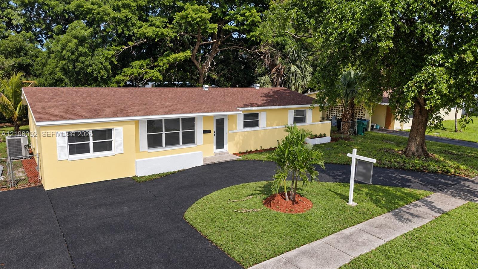 Single-story exterior featuring a stucco facade, curved asphalt driveway, white louvered shutters, and mature landscaping