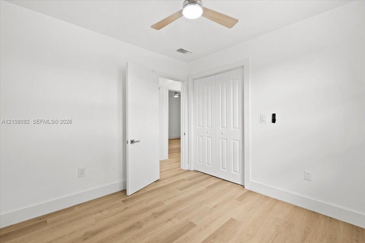 Neutral-toned room featuring wood-finish flooring, a ceiling fan with integrated lighting, a single-pane window, and white interior doors