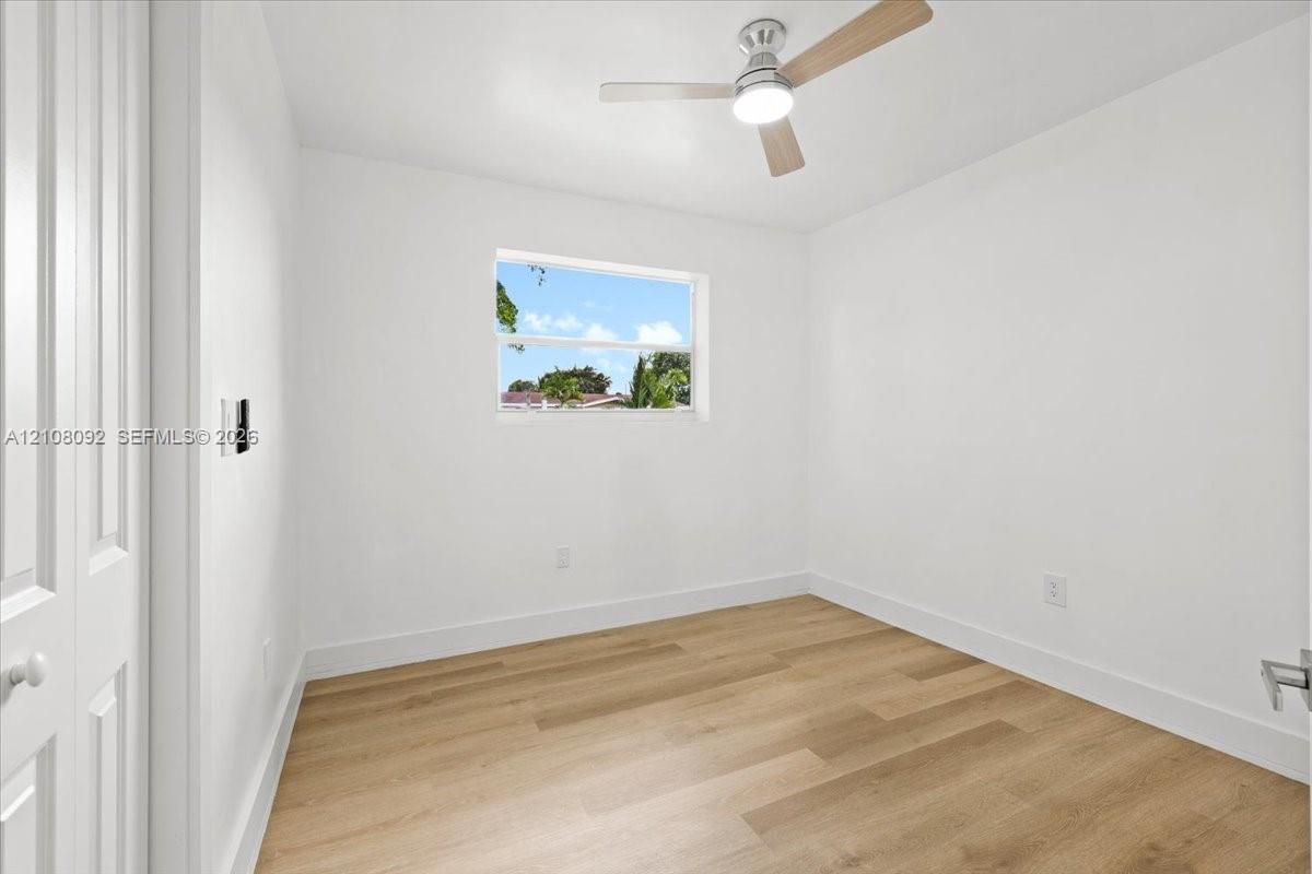 Neutral-toned interior featuring wood-finish flooring, a contemporary three-blade ceiling fan with integrated lighting, bi-fold closet doors, and solid-core interior doors