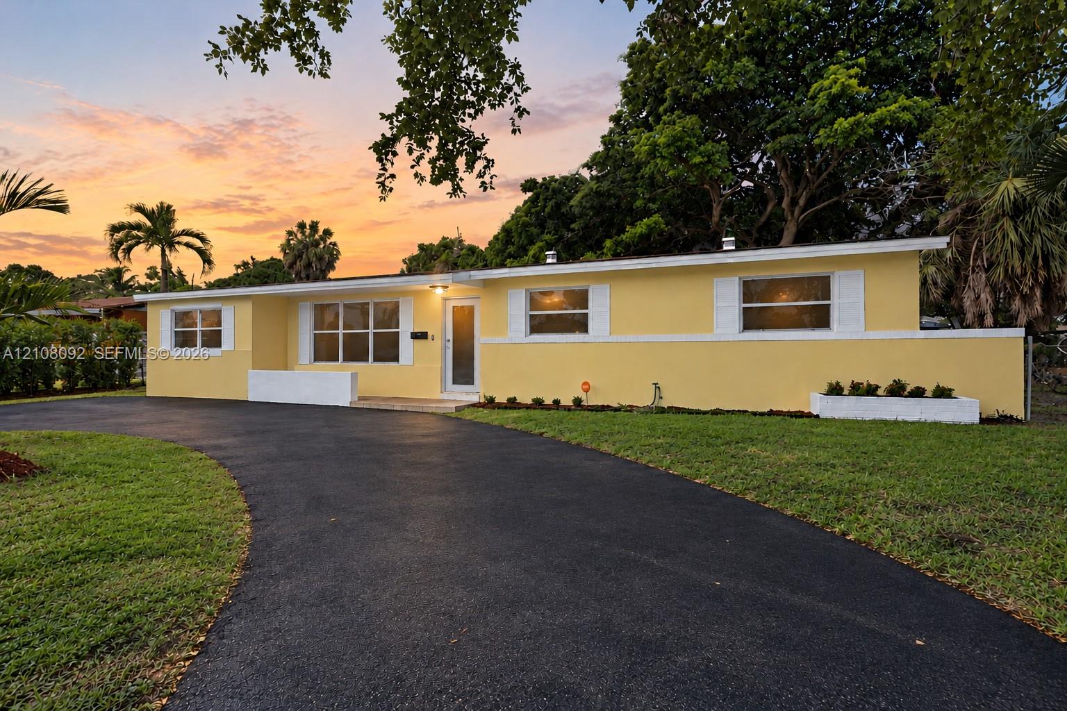 Single-story residence featuring a paved curved driveway, multi-pane windows with white exterior shutters, and mature trees