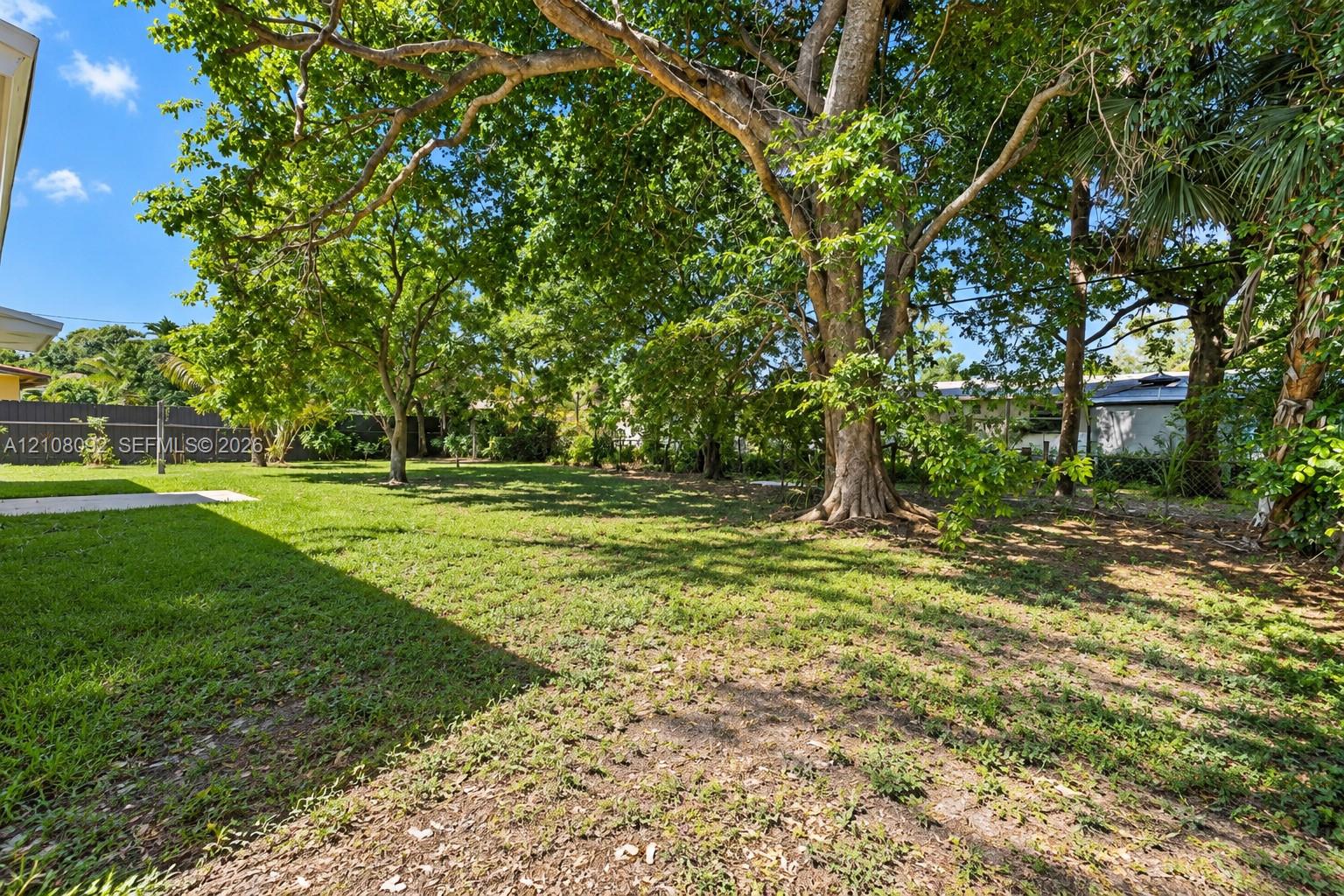 Spacious backyard featuring a manicured lawn, established mature trees, and a concrete patio area enclosed by perimeter fencing