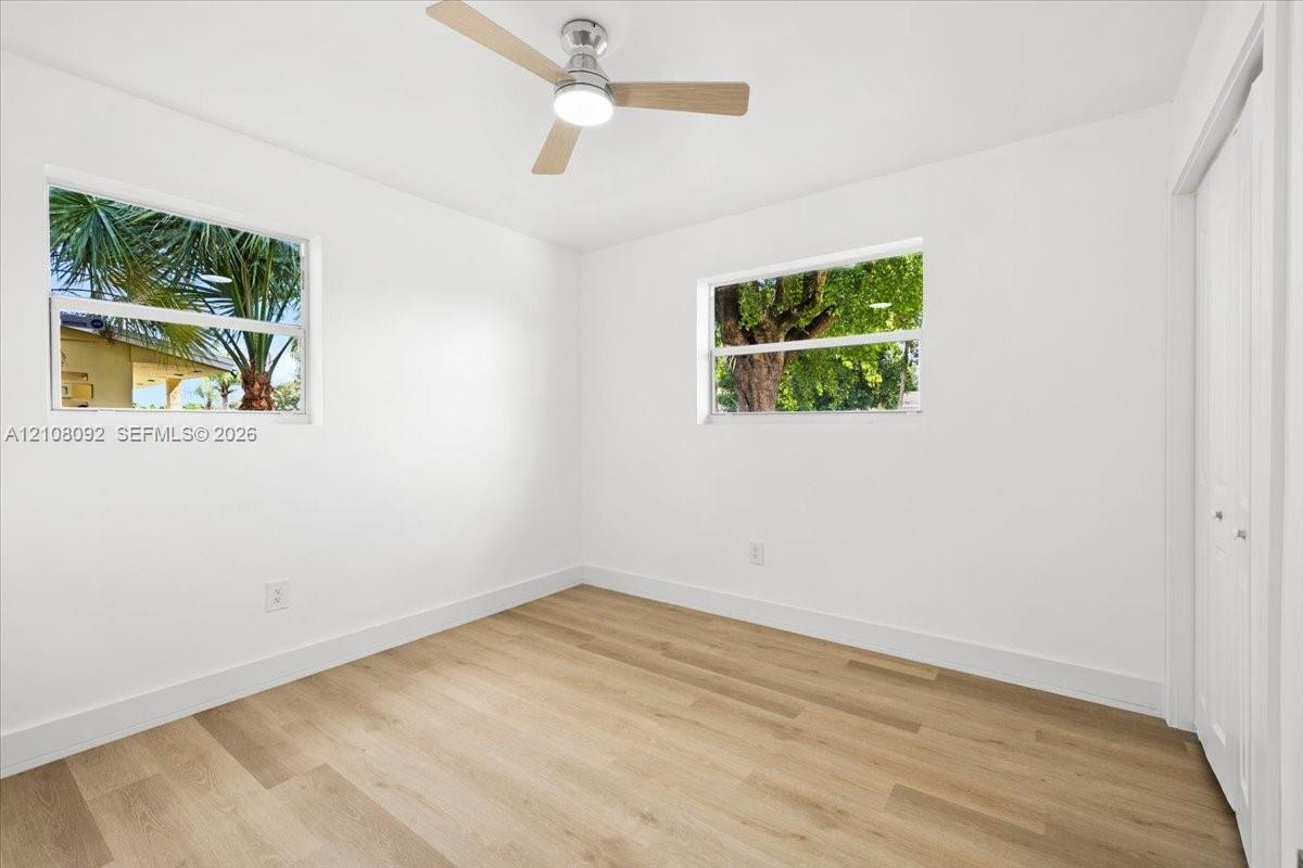 Interior space featuring wood-finish flooring, two dual-pane windows, a ceiling fan with integrated lighting, and a closet with bifold doors