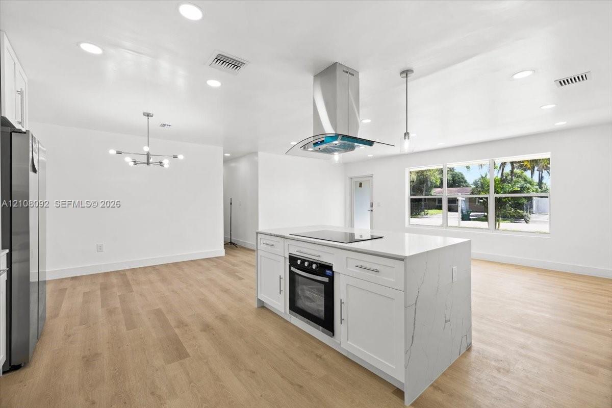 Kitchen featuring white cabinetry, solid-surface countertops, wood-finish flooring, recessed lighting, and a stainless steel range hood