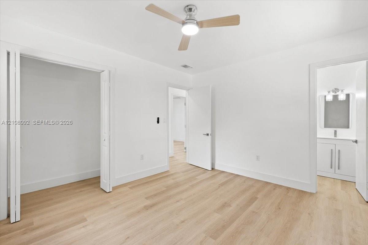 Neutral-toned interior featuring wood-finish flooring, a contemporary three-blade ceiling fan with integrated lighting, bi-fold closet doors, and solid-core interior doors