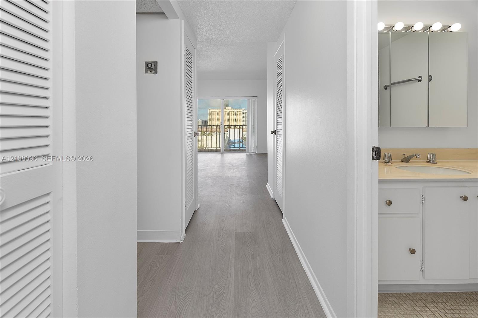 Hallway featuring wood-finish flooring, louvered closet doors, and sliding glass doors leading to a balcony