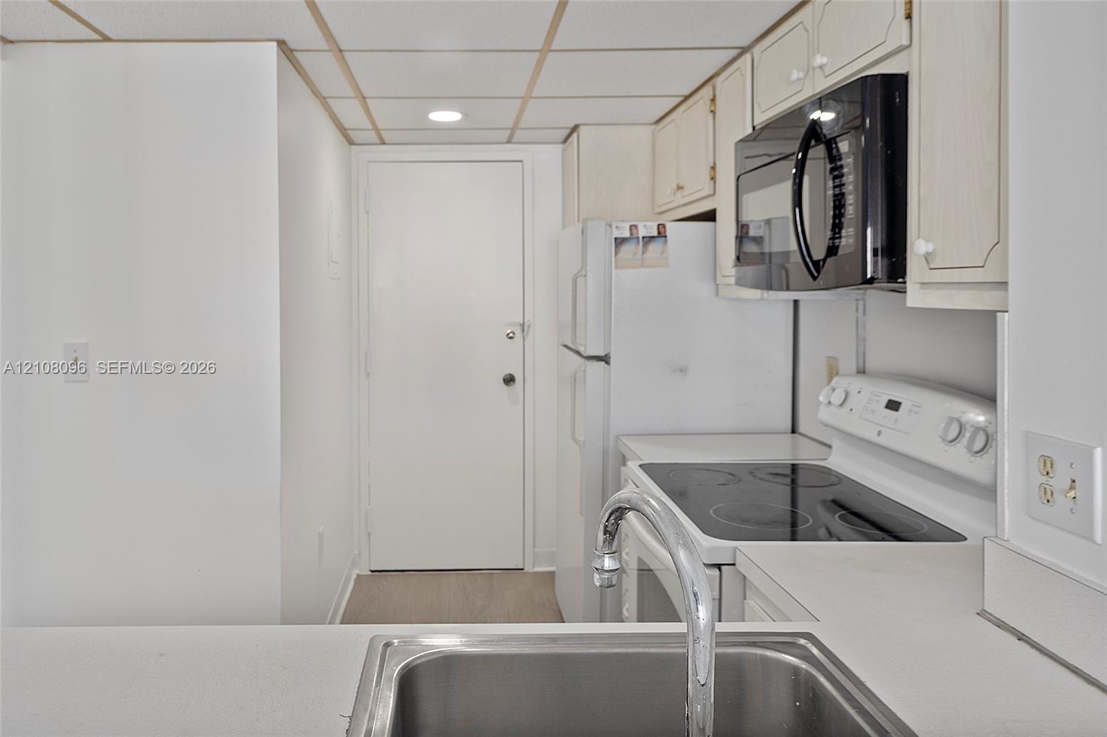 Kitchen featuring white cabinetry, an integrated microwave, a built-in electric range, and a stainless steel sink with a chrome faucet