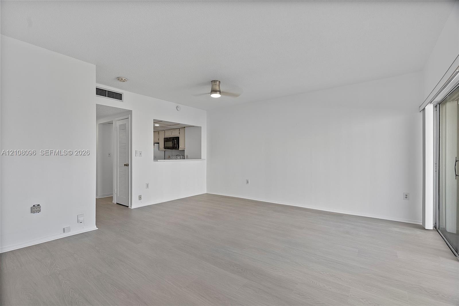 Open-concept interior featuring neutral wall tones, wood-finish flooring, a ceiling fan, and sliding glass doors