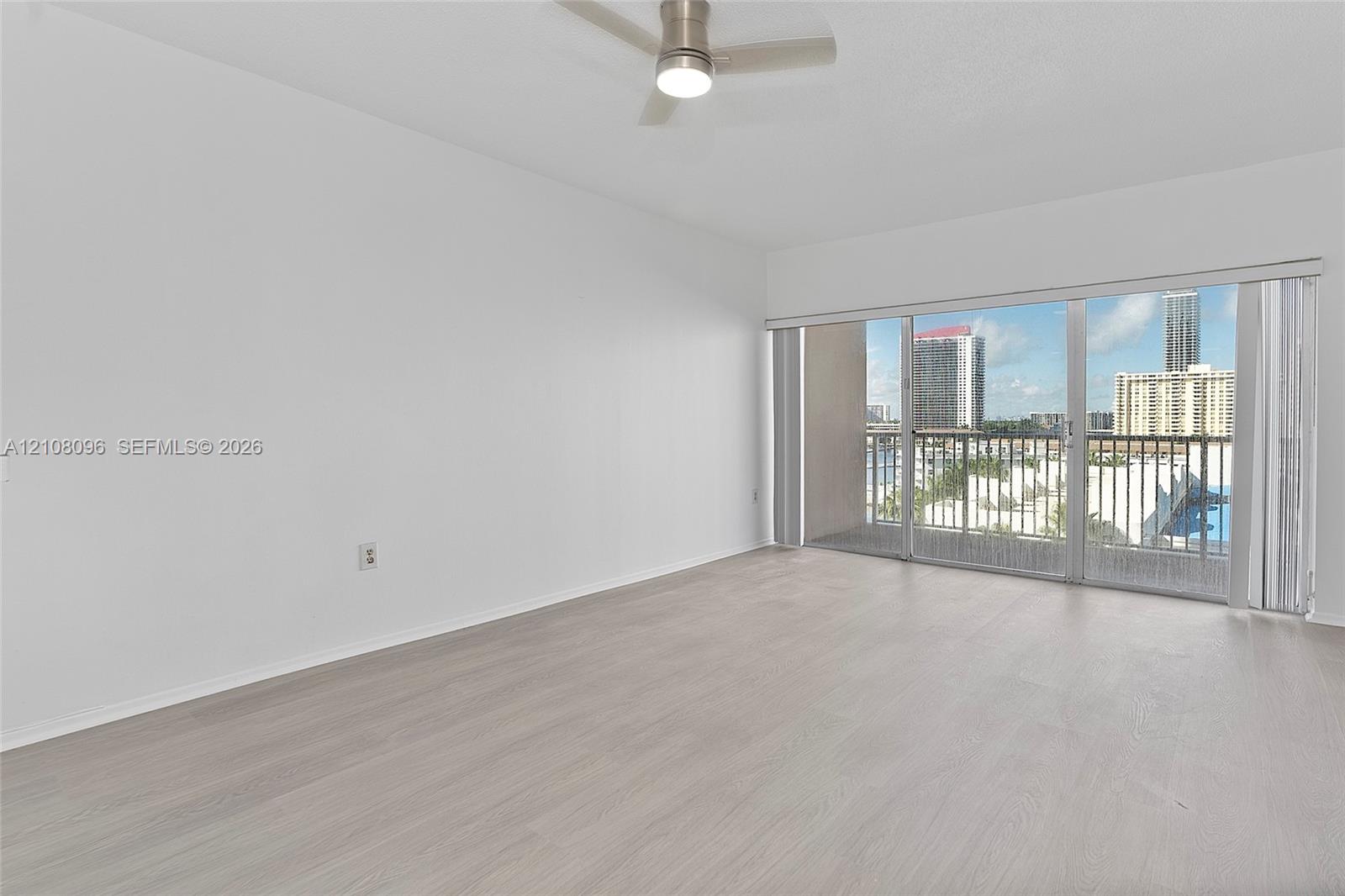 Neutral-toned wood-finish flooring, ceiling-mounted fan with integrated lighting, and full-height sliding glass doors opening to a private balcony