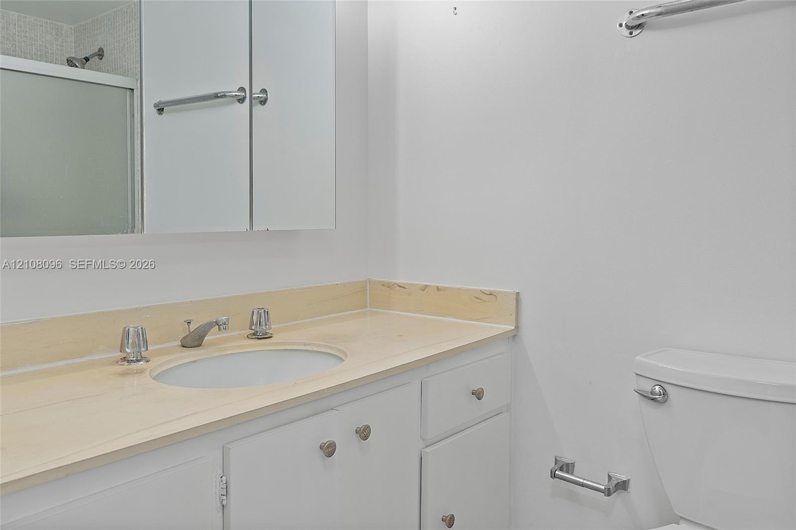 Bathroom featuring a light-toned solid surface vanity countertop, integrated sink, white cabinetry with metal hardware, wall-mounted medicine cabinet, and a framed glass shower enclosure