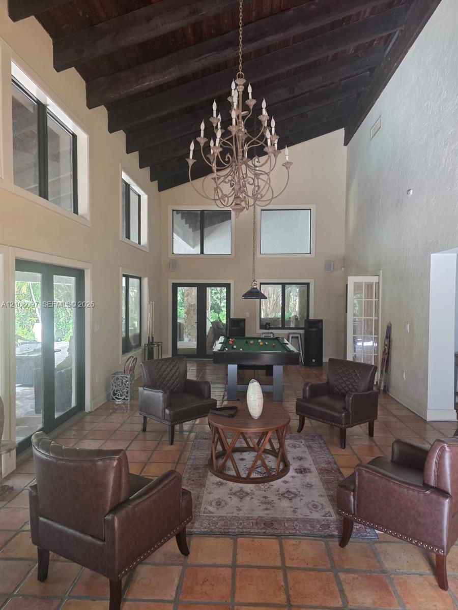 High vaulted ceilings with exposed dark wood beams, terracotta tile flooring, multi-light chandelier, and expansive windows
