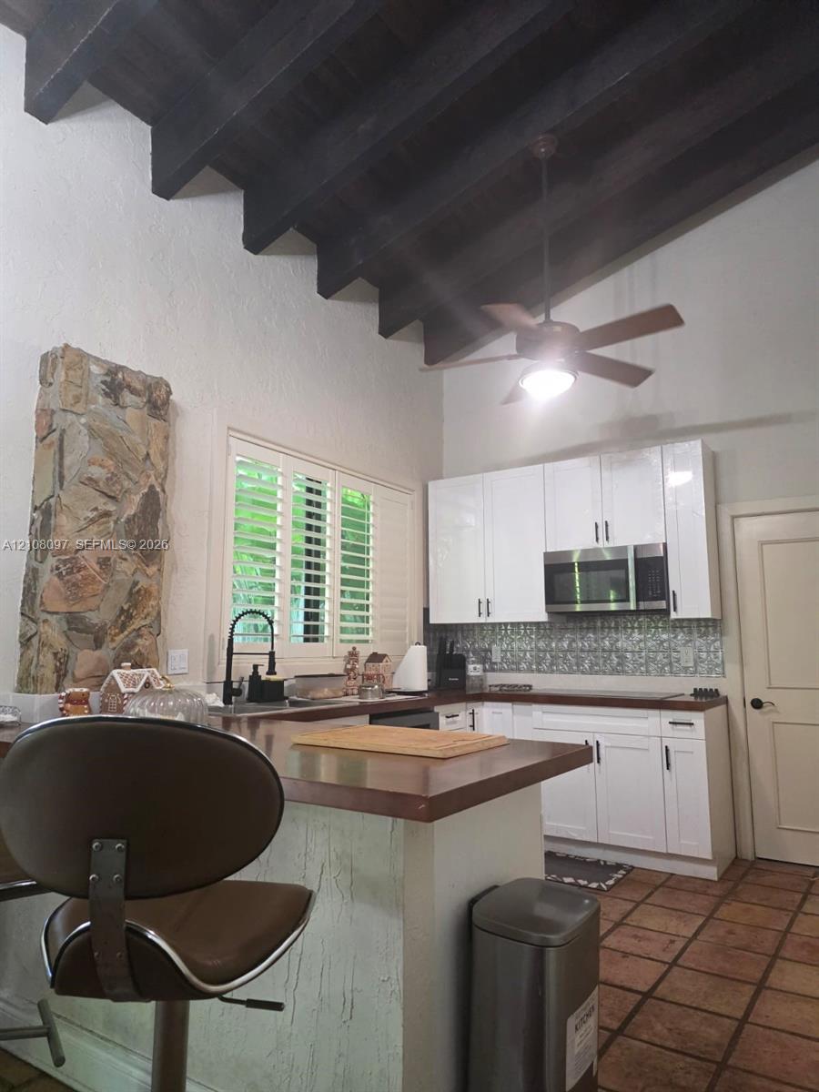 Kitchen featuring vaulted ceilings with exposed wood beams, stone accent wall, white cabinetry, tile flooring, and integrated countertop breakfast bar