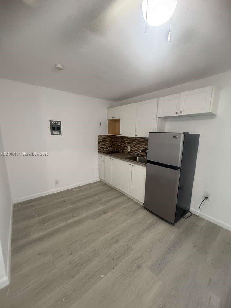 Kitchen featuring wood-finish flooring, white cabinetry, a multi-tonal decorative tile backsplash, and a stainless steel refrigerator