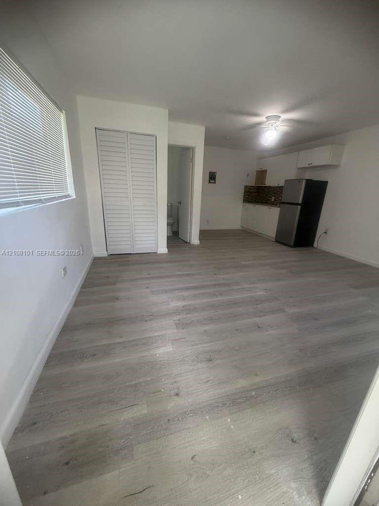 Open-concept space featuring wood-finish flooring, white cabinetry, a tiled backsplash, and louvered closet doors
