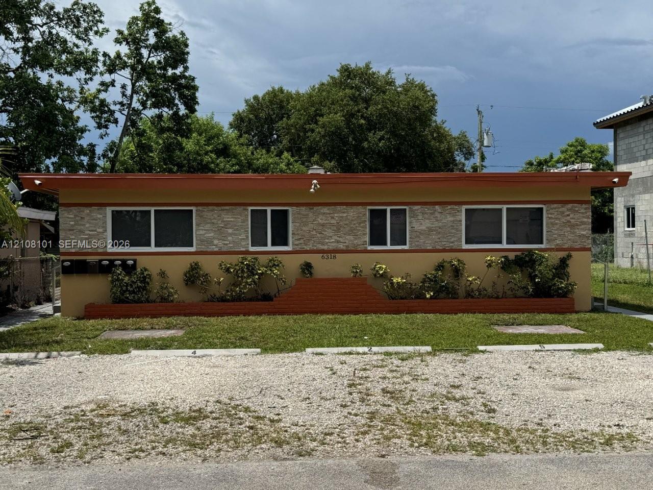 Single-story exterior featuring a stone-veneer facade, flat roofline, integrated brick planters, and designated gravel parking spaces