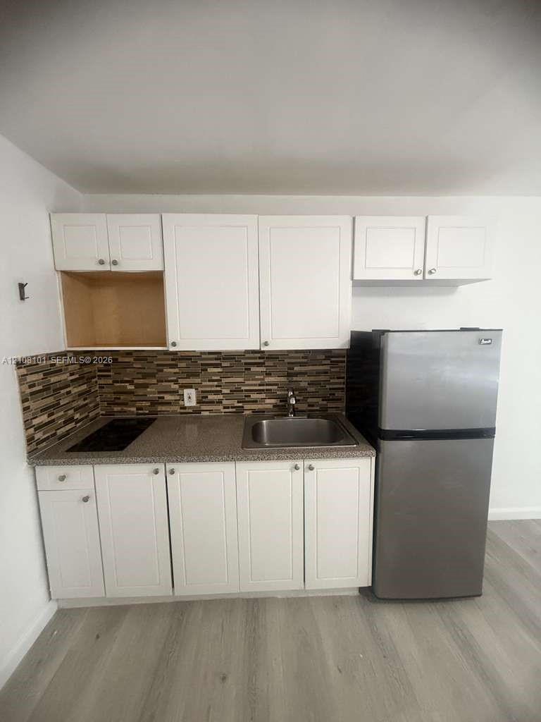 Kitchenette featuring white Shaker-style cabinetry, stone-texture countertops, mosaic tile backsplash, stainless steel sink, and wood-finish flooring