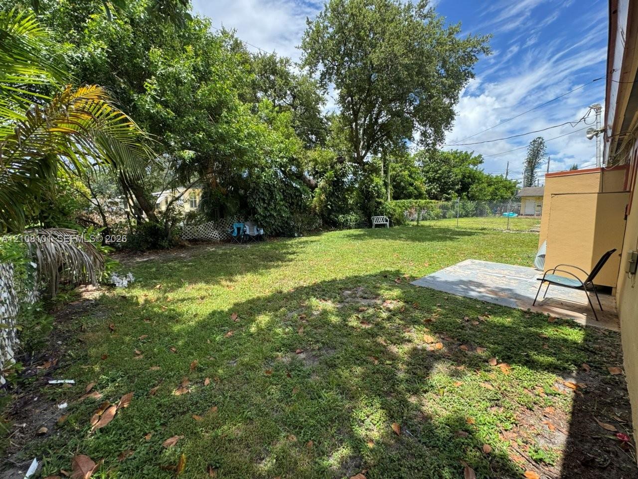 Backyard featuring a concrete patio, perimeter chain-link fencing, and mature trees