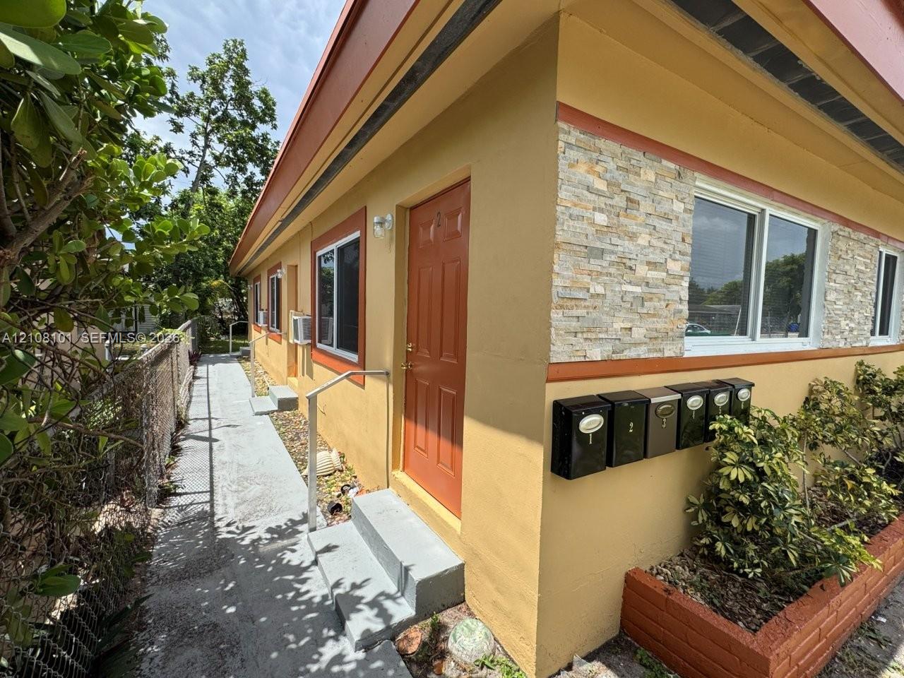 Exterior featuring a stucco facade with stacked stone veneer accents, multi-unit wall-mounted mailboxes, concrete steps with metal handrails, and a brick-lined landscape bed