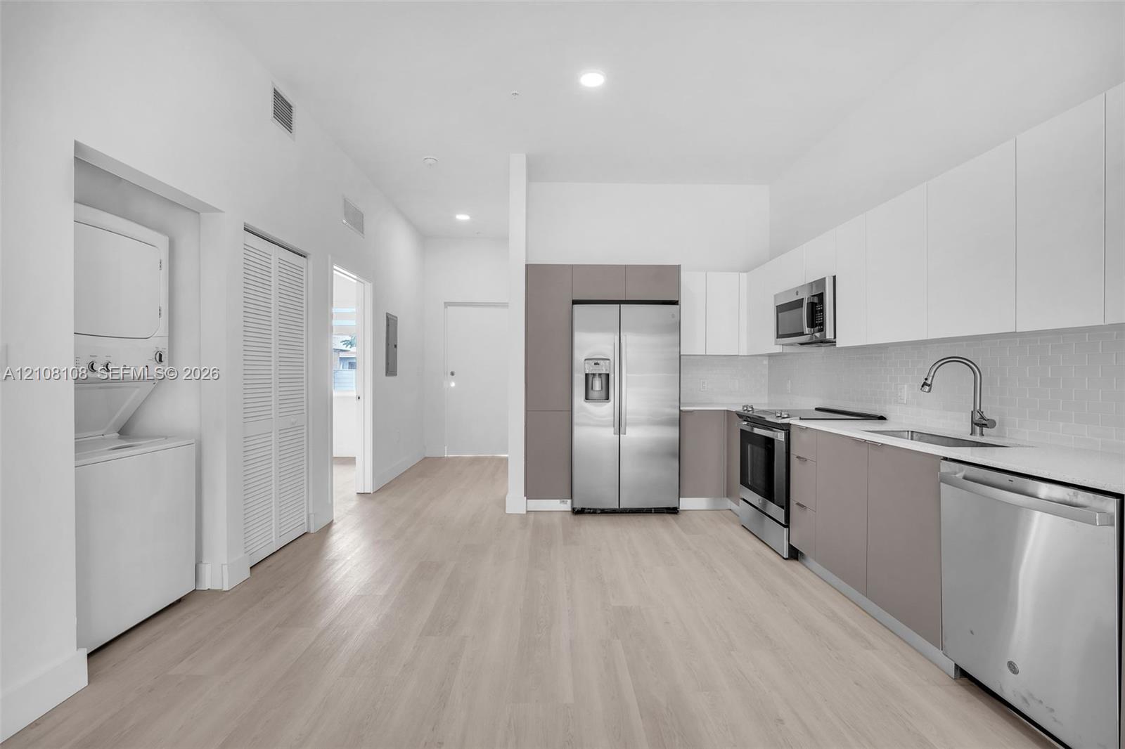 Kitchen featuring white and grey flat-panel cabinetry, stainless steel appliances, subway tile backsplash, and light-toned wood-finish flooring with an integrated laundry area Kitchen featuring white and grey flat-panel cabinetry, stainless steel appliances, subway tile backsplash, and light-toned wood-finish flooring with an integrated laundry area