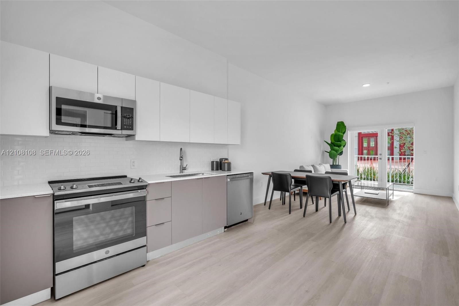 Kitchen featuring two-tone flat-panel cabinetry, stainless steel appliances, white subway tile backsplash, quartz countertops, and wood-finish flooring Kitchen featuring two-tone flat-panel cabinetry, stainless steel appliances, white subway tile backsplash, quartz countertops, and wood-finish flooring