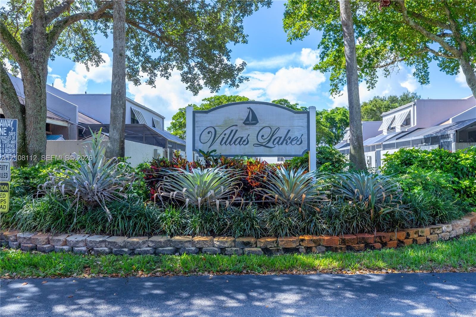 Community signage featuring mature canopy trees, sculpted landscaping, and a masonry border wall