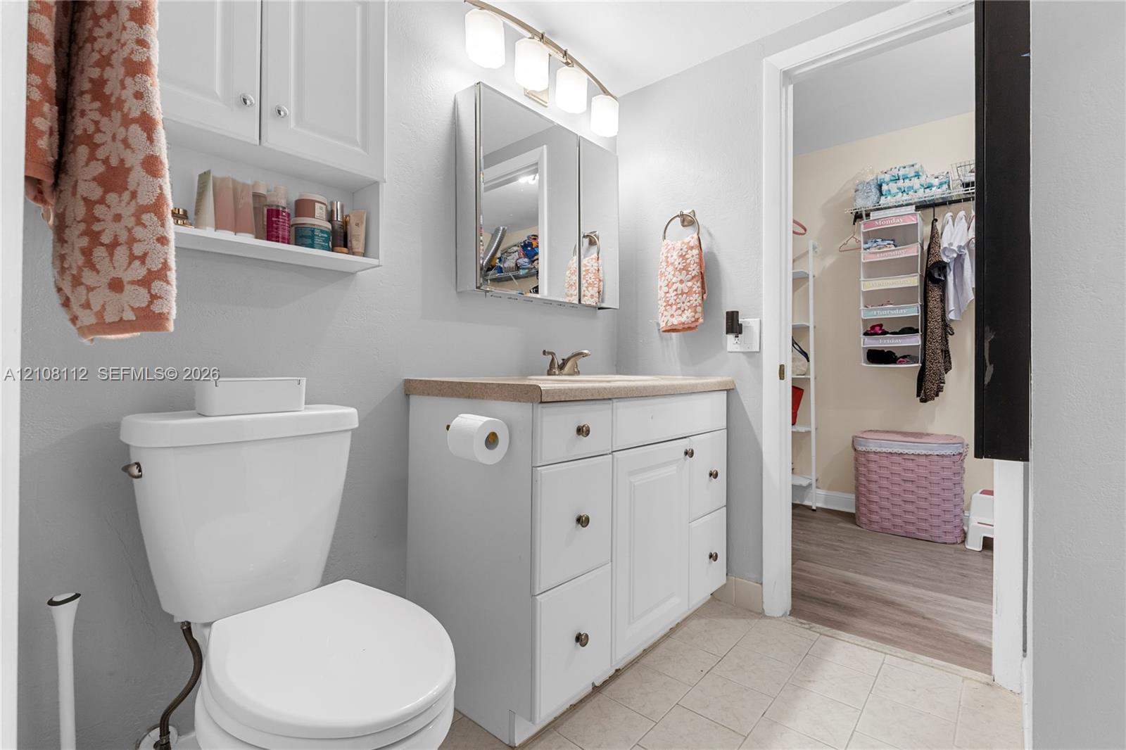 Bathroom featuring white cabinetry, a tri-panel medicine cabinet, wall-mounted light fixture, and solid surface countertop with an integrated sink