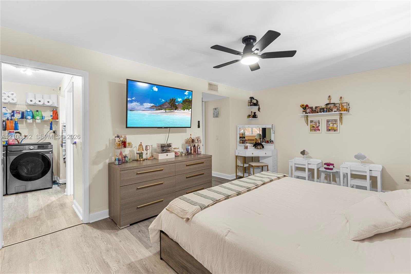 Neutral-toned room featuring wood-finish flooring, a ceiling fan with integrated lighting, and an attached laundry area with built-in shelving