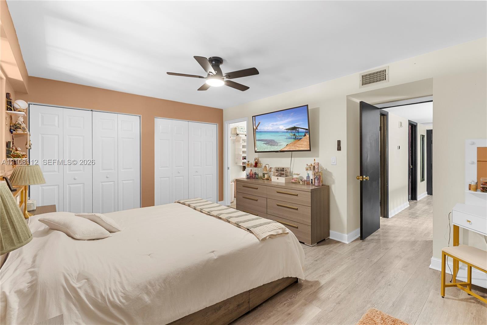 Neutral-tone interior space featuring wood-finish flooring, dual sets of bi-fold closet doors, and a ceiling fan with integrated lighting