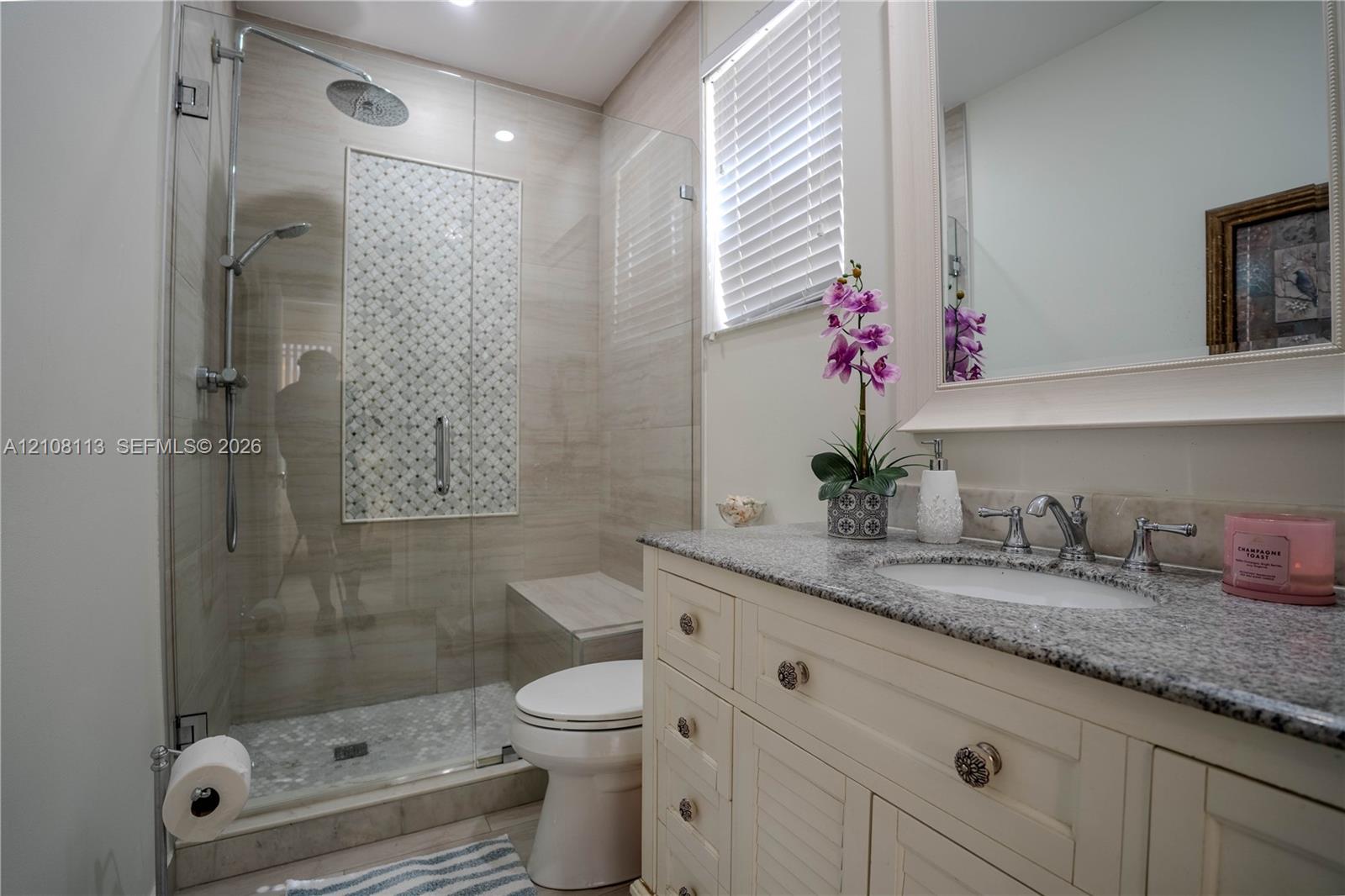 Bathroom featuring a vanity with stone-finish countertop, undermount sink, walk-in glass-enclosed shower with tiled accent inlay, and built-in shower bench